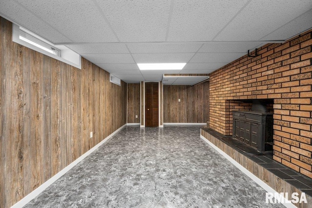 finished basement featuring wooden walls, a paneled ceiling, baseboards, and a wood stove