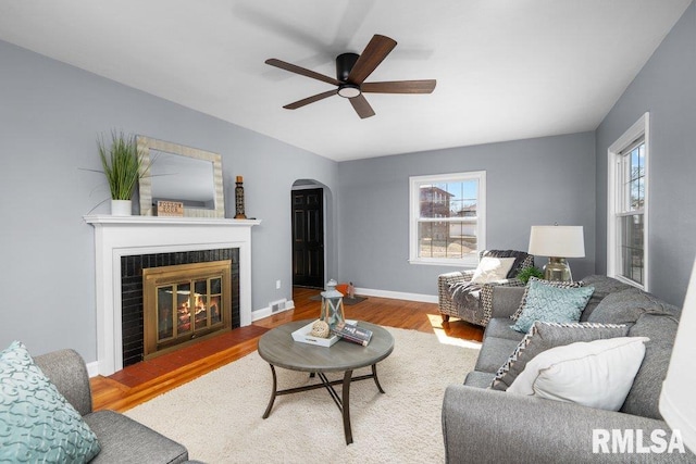 living area featuring a wealth of natural light, arched walkways, wood finished floors, and a fireplace with flush hearth