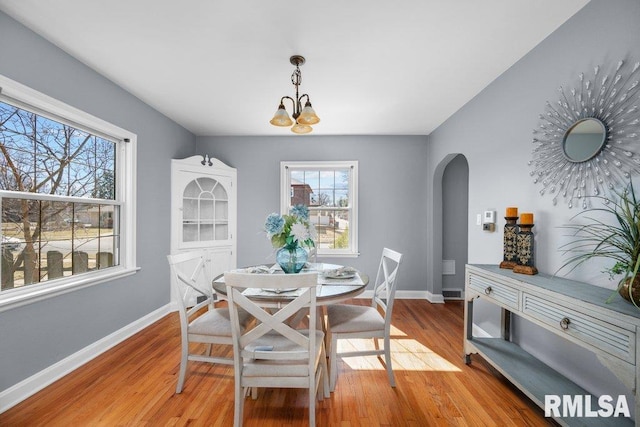 dining space with light wood-type flooring, visible vents, a notable chandelier, arched walkways, and baseboards