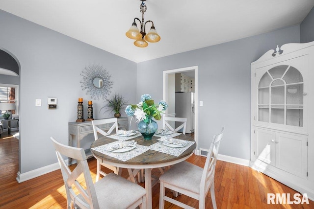 dining area with light wood-type flooring, arched walkways, and baseboards