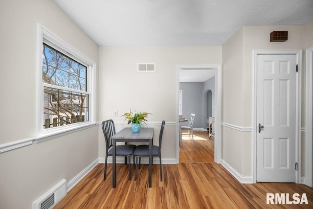 dining room with visible vents, baseboards, arched walkways, and wood finished floors