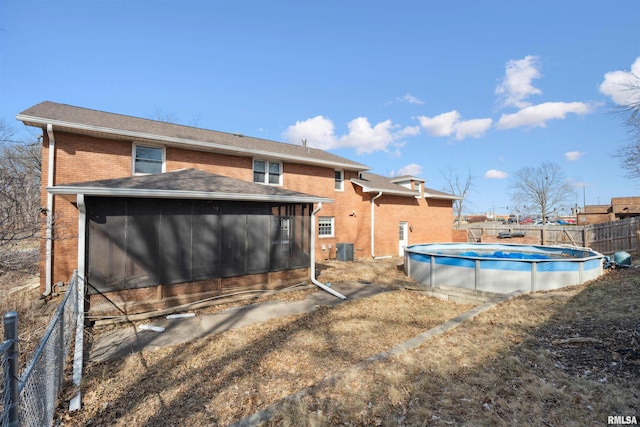 rear view of house with fence, a fenced in pool, central AC, a sunroom, and brick siding