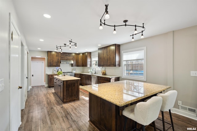 kitchen with decorative backsplash, a kitchen island, dark brown cabinets, and range hood