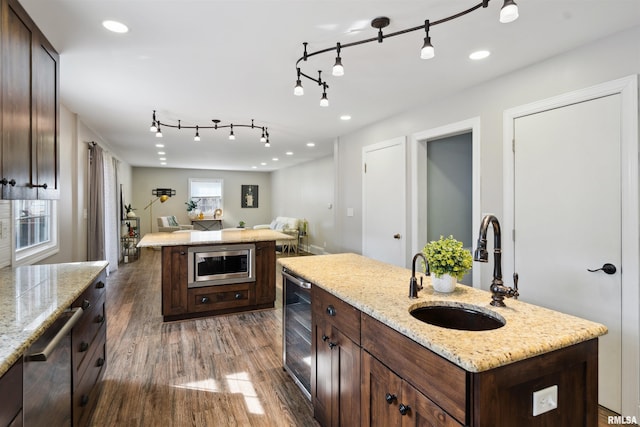 kitchen with beverage cooler, dark wood finished floors, an island with sink, stainless steel appliances, and a sink