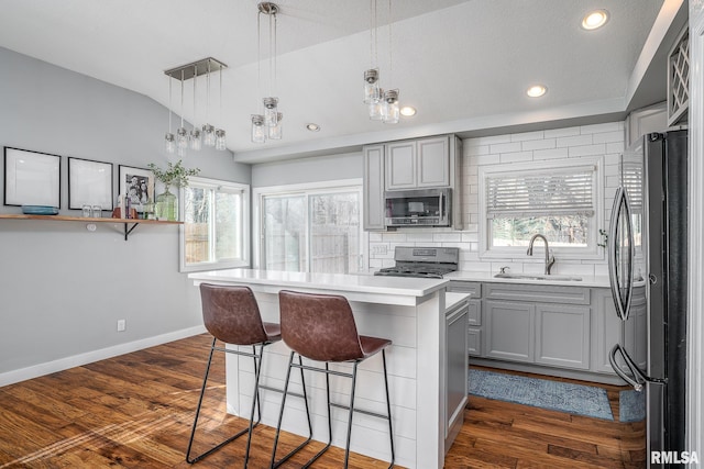 kitchen with gray cabinetry, a kitchen bar, vaulted ceiling, stainless steel appliances, and a sink