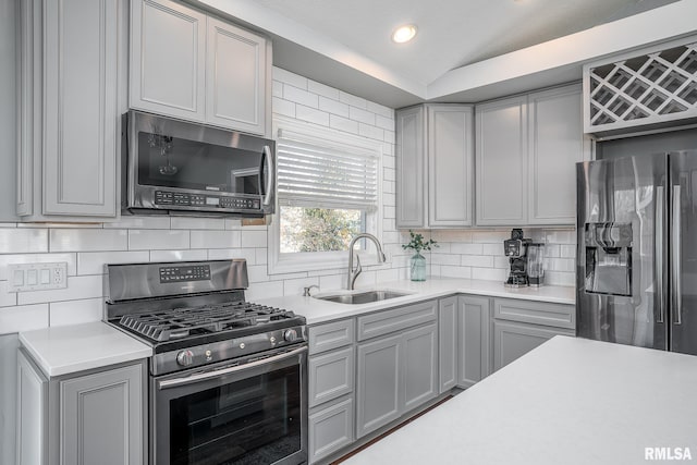 kitchen with gray cabinetry, a sink, light countertops, vaulted ceiling, and appliances with stainless steel finishes