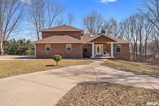 view of front of house with brick siding, a shingled roof, a front lawn, concrete driveway, and a chimney