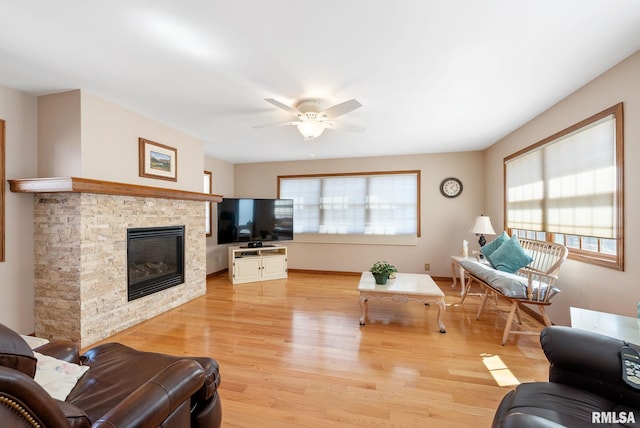 living area with a stone fireplace, light wood-style flooring, baseboards, and a ceiling fan