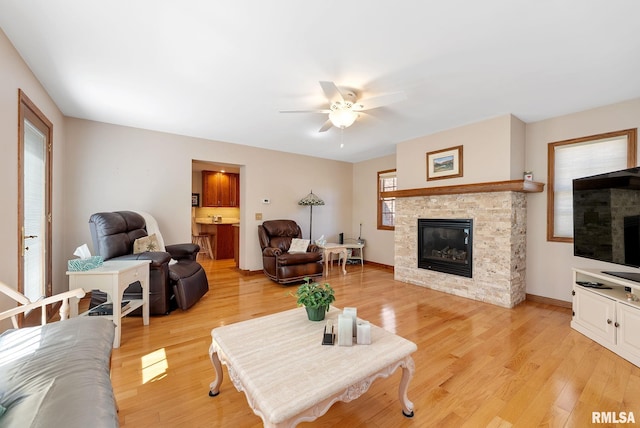 living area featuring light wood-style flooring, a fireplace, baseboards, and a ceiling fan