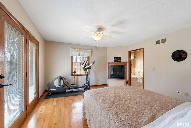 bedroom with visible vents, light wood-style flooring, a textured ceiling, and a glass covered fireplace