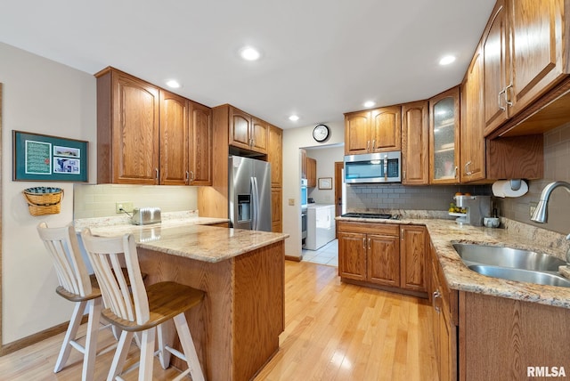 kitchen featuring a sink, stainless steel appliances, a peninsula, a breakfast bar area, and light stone countertops