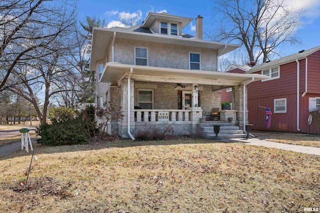 american foursquare style home featuring stucco siding, stone siding, a porch, and a chimney