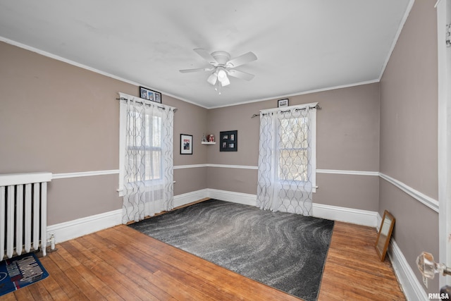 spare room featuring radiator, wood finished floors, baseboards, a healthy amount of sunlight, and crown molding