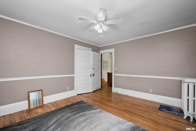 unfurnished room with radiator, crown molding, ceiling fan, baseboards, and wood finished floors