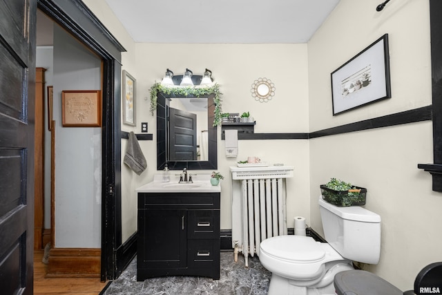 half bath with radiator, toilet, vanity, and wood finished floors