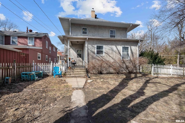 rear view of house with stucco siding, a chimney, and fence