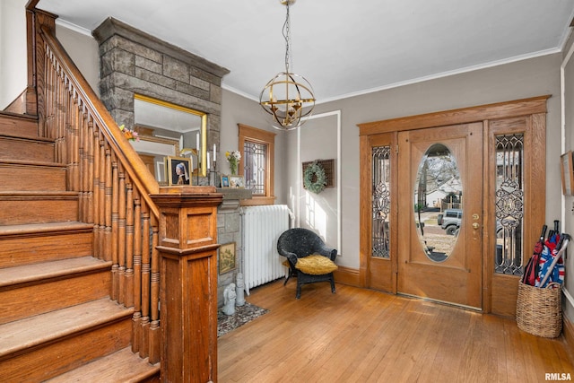 foyer featuring light wood finished floors, radiator, stairway, ornamental molding, and an inviting chandelier