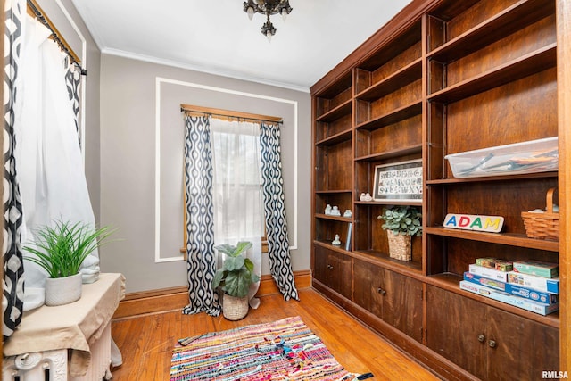 living area with light wood-type flooring, baseboards, and crown molding