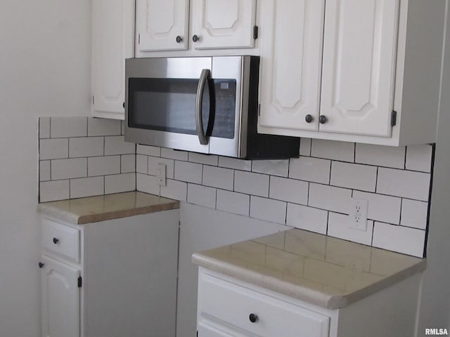 kitchen featuring stainless steel microwave, backsplash, and white cabinetry