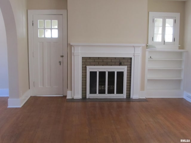 unfurnished living room with wood finished floors, a fireplace, arched walkways, and baseboards