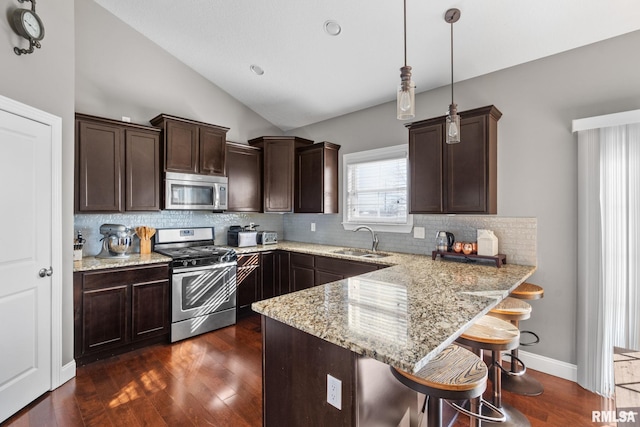 kitchen with a peninsula, lofted ceiling, a sink, stainless steel appliances, and dark brown cabinetry