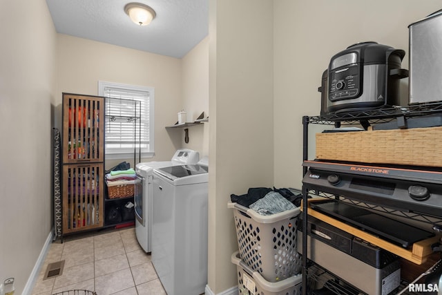 clothes washing area with baseboards, visible vents, laundry area, light tile patterned flooring, and washer and clothes dryer