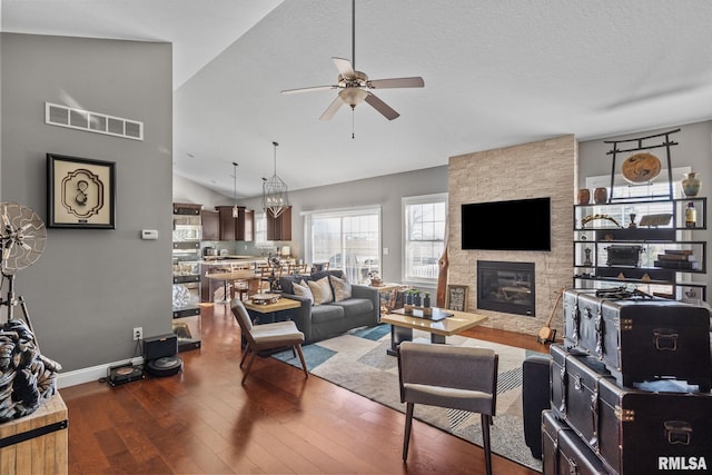 living room featuring hardwood / wood-style floors, visible vents, lofted ceiling, a fireplace, and ceiling fan