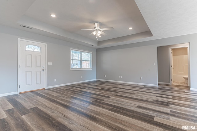 interior space featuring dark wood finished floors, a tray ceiling, and baseboards