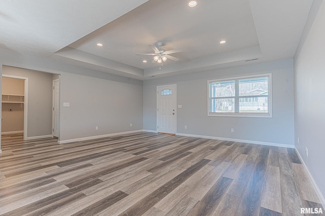 unfurnished living room featuring a raised ceiling, baseboards, and wood finished floors