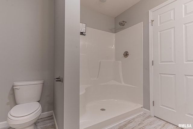 bathroom featuring baseboards, toilet, walk in shower, and wood finished floors