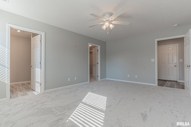 unfurnished bedroom featuring a walk in closet, baseboards, a ceiling fan, and carpet flooring