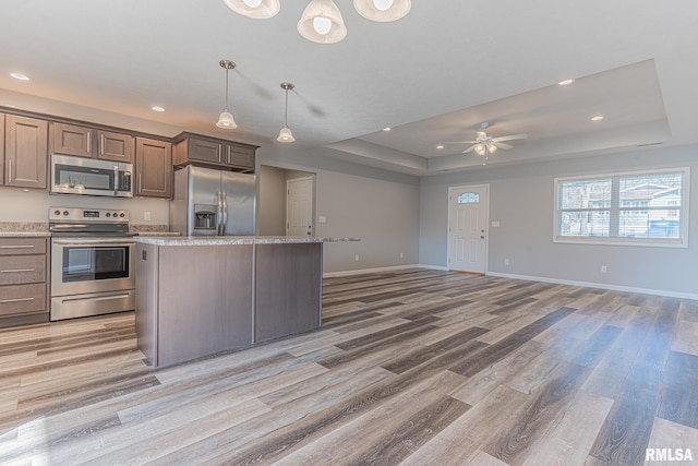 kitchen with a raised ceiling, a kitchen island, appliances with stainless steel finishes, light wood finished floors, and baseboards