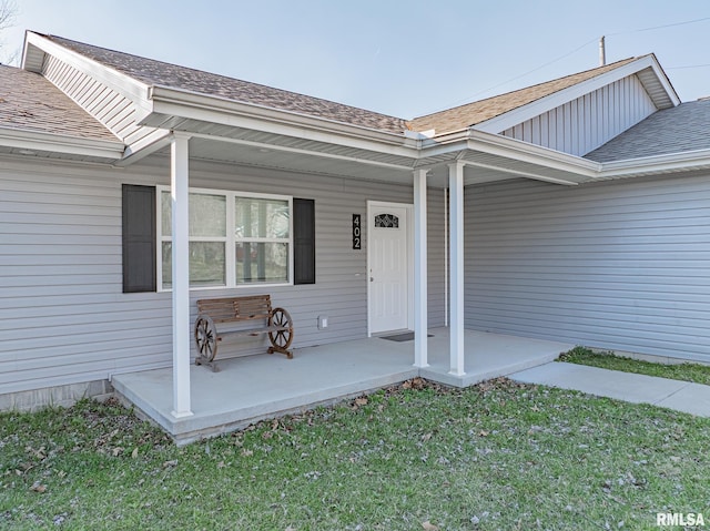 view of exterior entry with a lawn, a porch, and a shingled roof