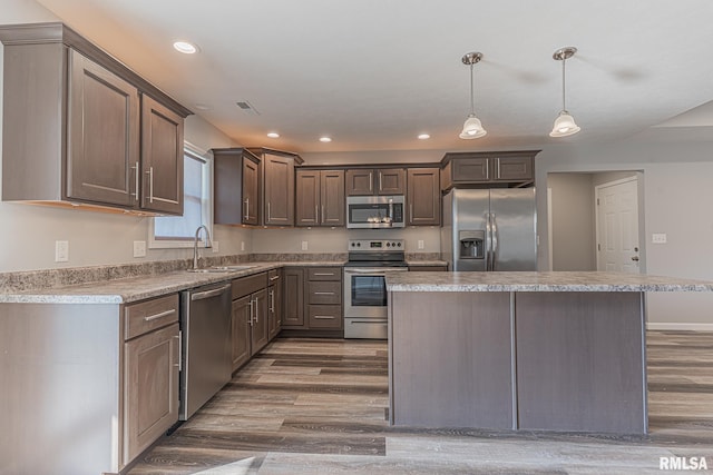 kitchen with visible vents, a kitchen island, appliances with stainless steel finishes, wood finished floors, and a sink