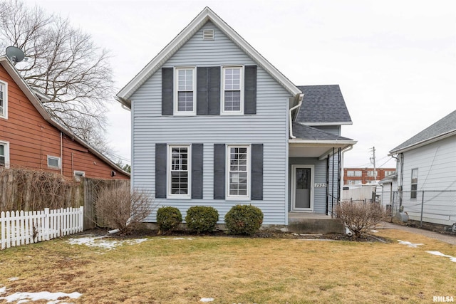 traditional-style home with roof with shingles, a front yard, and fence