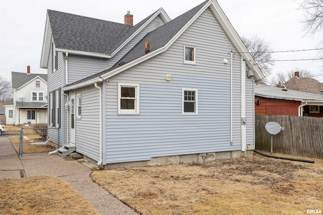 view of home's exterior featuring fence, roof with shingles, a chimney, and entry steps