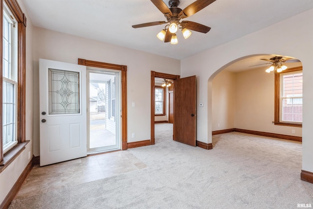 entryway featuring arched walkways, ceiling fan, baseboards, and carpet