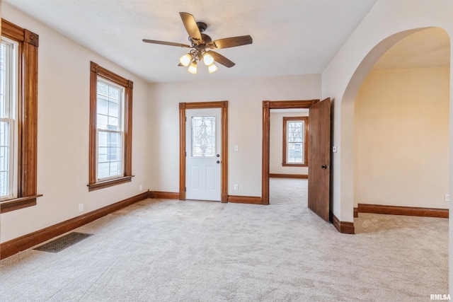 foyer featuring visible vents, baseboards, light carpet, arched walkways, and a ceiling fan