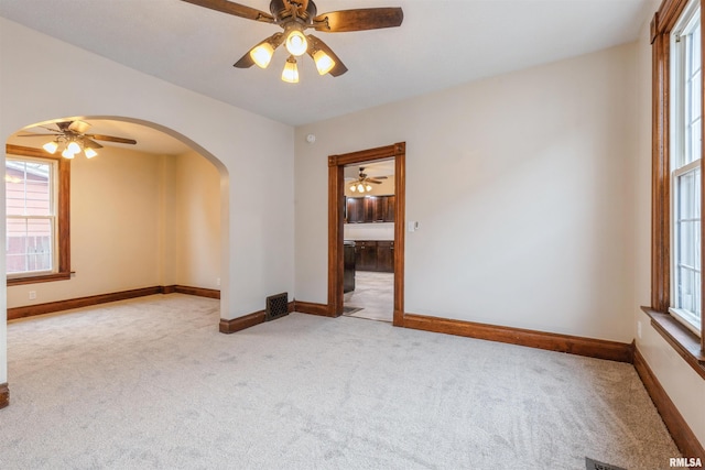 unfurnished room with a wealth of natural light, baseboards, arched walkways, and carpet floors