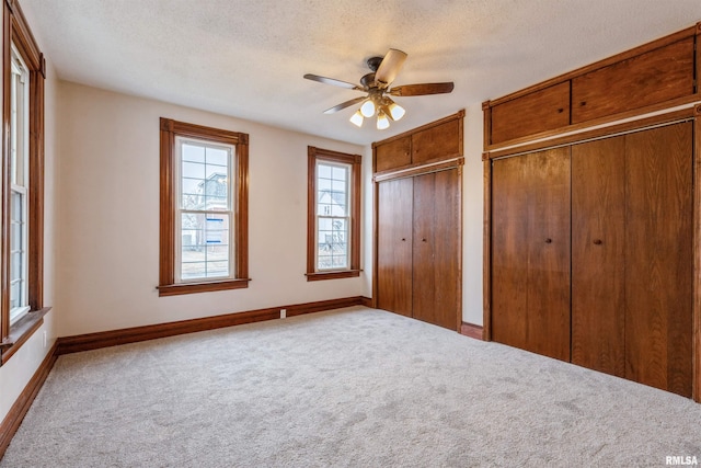 unfurnished bedroom featuring baseboards, carpet floors, a textured ceiling, and multiple closets