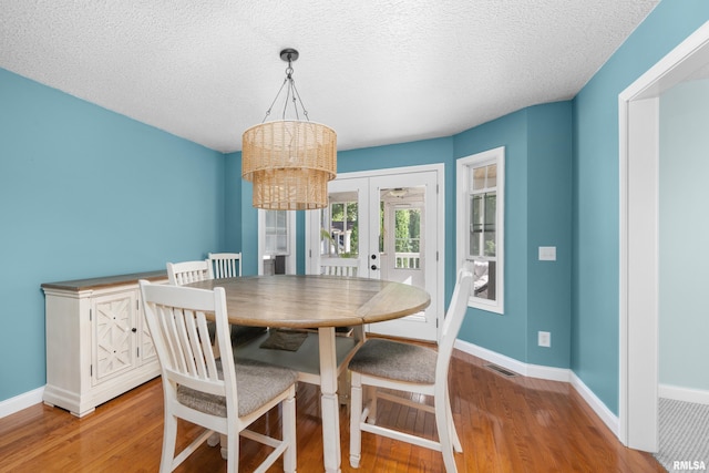 dining area featuring wood finished floors, visible vents, baseboards, french doors, and a textured ceiling