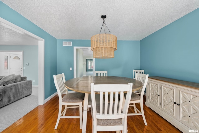 dining area with visible vents, a textured ceiling, baseboards, and wood finished floors