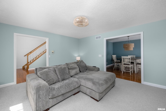 living area featuring visible vents, a textured ceiling, stairway, carpet floors, and baseboards