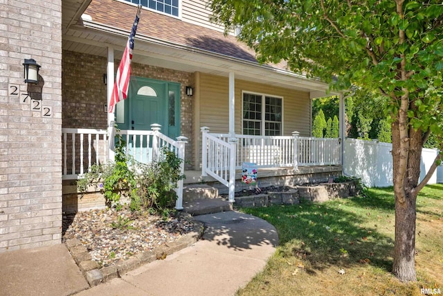 entrance to property with a yard, brick siding, covered porch, and roof with shingles