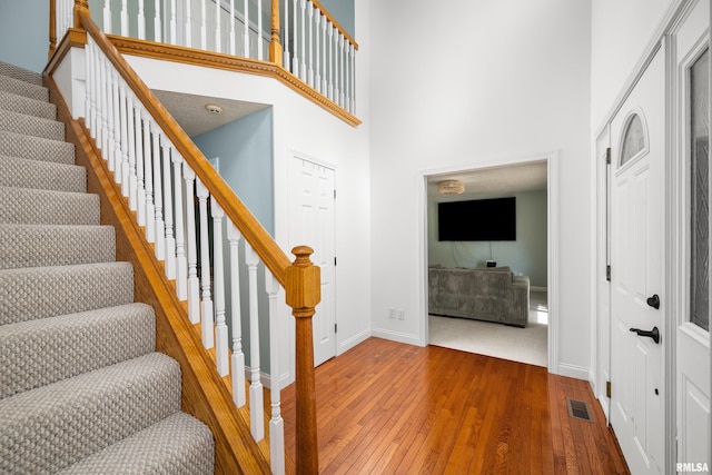 entrance foyer with wood finished floors, visible vents, baseboards, a high ceiling, and stairs