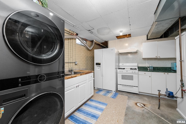 kitchen with stacked washer and dryer, under cabinet range hood, a sink, white appliances, and concrete floors