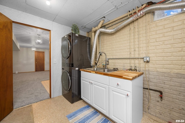 washroom with brick wall, light colored carpet, stacked washer and clothes dryer, cabinet space, and a sink