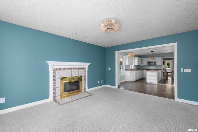 unfurnished living room with dark carpet, a fireplace, a textured ceiling, and baseboards