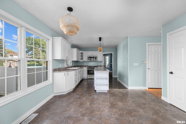 kitchen with a kitchen island, stainless steel appliances, white cabinets, baseboards, and hanging light fixtures