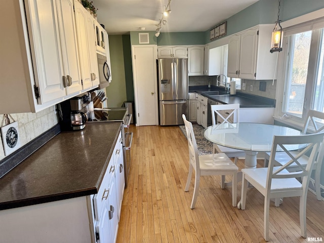 kitchen featuring light wood-style flooring, a sink, dark countertops, appliances with stainless steel finishes, and decorative backsplash